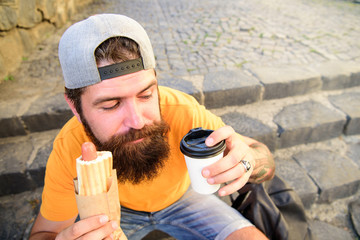 Tasty sausage in roasty bun. Urban food culture concept. Hipster eat hot dog while sit on stairs...