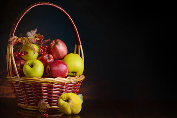 Wicker basket with autumn fruits of apples, quince and viburnum on a dark background. Beautiful autumn still life. Place for your text