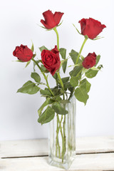 A bouquet of scarlet roses in a glass vase. Five flowers. On a white background