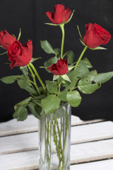 A bouquet of scarlet roses in a glass vase. Five flowers. On a black background