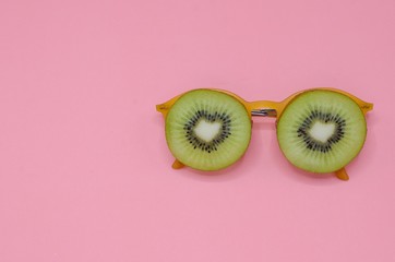Two slice green kiwi fruits put on yellow sunglasses set as face with eyes photo isolated on pink...