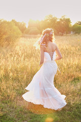 Young girl in a white dress in the meadow. Woman in a beautiful long dress posing in the garden. Stunning bride in a wedding dress