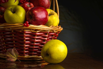 Wicker basket with autumn fruits of apples, quince and viburnum on a dark background. Beautiful autumn still life. Place for your text