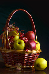 Wicker basket with autumn fruits of apples, quince and viburnum on a dark background. Beautiful autumn still life