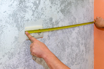 construction work, a worker measures the wall with a building tape measure