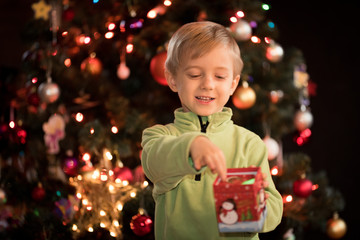 5 years old boy lies in front of the Christmas tree and looks at the  colorful lights and candle