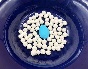 One turquoise sugared almond or comfit on blue ceramic background with white small sugar candy.