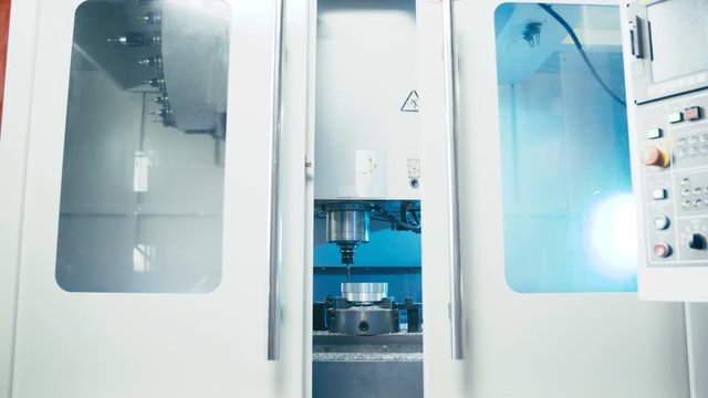 Door open to CNC milling machine making product 4K. Zooming in to milling machine with doors in focus automatically open. Industrial process.