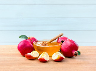 Honey in glass bowl, wooden honey dipper, red apples and garnet on wooden table on a blue wooden...
