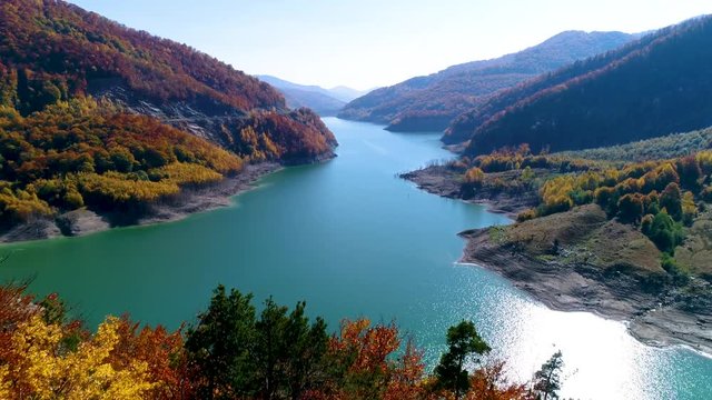 Aerial View. Autumn color forest. Colorful autumn trees, turquoise lake on a sunny fall day. Beautiful Lake in the mountains surrounded by colorful autumn forest. Crystal clear water of the lake. 