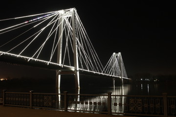 Night illumination on the cable-stayed bridge over the river.