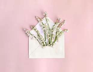 Wall murals Lily of the valley Beautiful flowers white lily of the valley ( Convallaria majalis, lily-of-the-valley, May bells, Mary's tears ) in postal envelope on a pink paper background. Top view, flat lay
