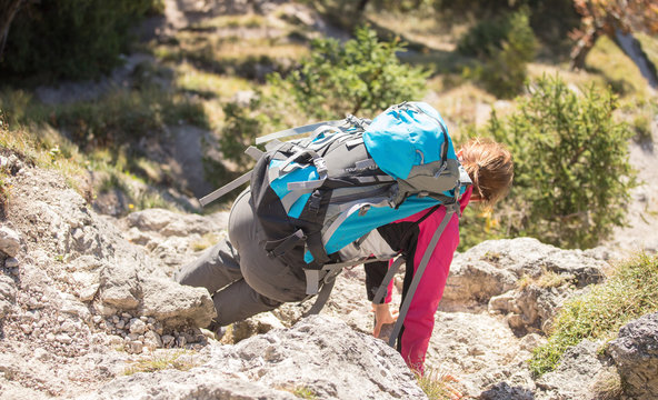 Junge Frau mit Wanderrucksack klettert den Fels hinab
