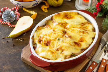 Potato gratin with pear, raclette cheese, and bacon on a festive Christmas table.Traditional french cuisine. Copy space.