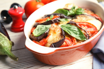 Baked eggplant with tomatoes, cheese and basil in dishware on table, closeup
