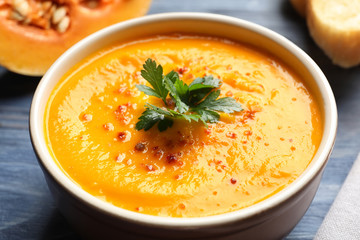 Delicious pumpkin cream soup with parsley and spices in bowl on table, closeup