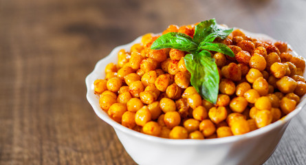 Fried spicy chickpeas in white bowl on wooden table background