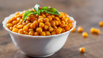 Fried spicy chickpeas in white bowl on wooden table background