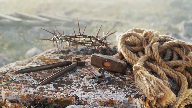Close up of a representation of the Jesus Christ crown of thorns with nails, hammer, pliers and a rope placed on a stone.
