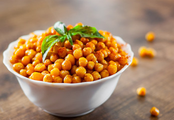 Fried spicy chickpeas in white bowl on wooden table background