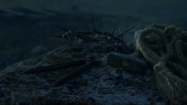 Close up of a representation of the Jesus Christ crown of thorns with nails, hammer, pliers and a rope placed on a stone.