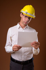 Portrait of businessman wearing hardhat against brown background
