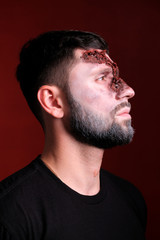 Fototapeta premium A man looks to the side with a wound on the floor of his face against a darkened red background.