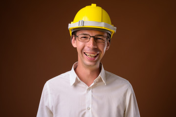 Portrait of businessman wearing hardhat against brown background