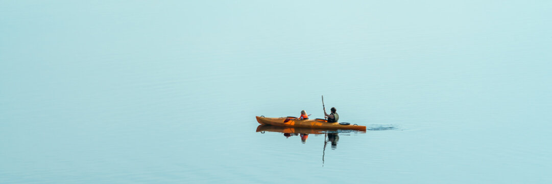 Two people kayaking on a calm lake, panorama