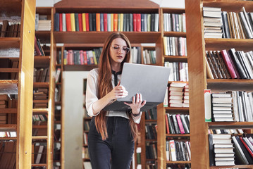 Young beautiful woman is a student at a library with her laptop