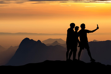 silhouette of people taking selfie at the cliff on mountains with sunset in the evening