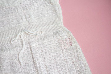 White baby's knitted clothes on pink background.