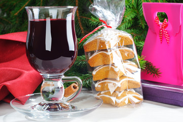 Mulled wine with cinnamon sticks in glass and cookies on the wooden table with christmas tree branch on background