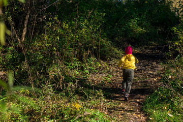 A little girl, a child, in warm clothes and a red cap runs away along the path in the dark autumn...
