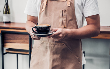 asian male barista wear apron holding hot coffee cup served to customer with smiling face at bar counter,Cafe restaurant service concept.waitress working.