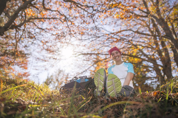 Naklejka na ściany i meble Junge sportliche Frau sitzt im Gras, Blätterdach aus bunten Blättern, Wanderschuhe im Vodergrund, Herbst