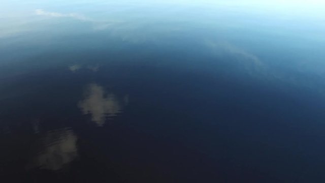 A shot of a shallow lake gently rippling with blue sky and clouds reflecting on the water surface