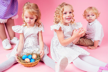 three little blonde child with a chick cock easter in studio pink background.beautiful boy and girls kids celebrating Easter Holiday with pets, painted eggs in wicker basket.dream birthday present