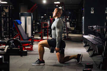 Fototapeta na wymiar Brutal muscular man doing sport exercises with dumbbells in the gym. A strong guy is engaged in fitness. Concept sport, health