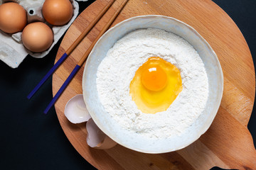 Food preparation for homemade dough for pasta or Chinese egg noodles by organic eggs and all purpose flour in a ceramic bowl with copy space.