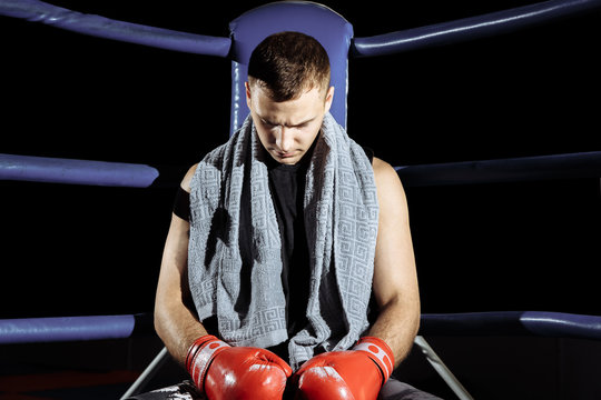 Muscular professional kick boxer resting on the ropes in the corner of the ring while training for the next match.
