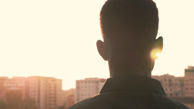 urbanization, city, suburbs. Young African man contemplates the city at sunset