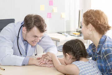 Obraz premium Pediatrician (doctor) man giving fist bump (High Five To),reassuring and discussing kid at surgery.Mother Caucasian and kid smiling in hospital room.Copy space.