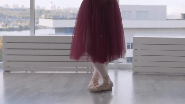 Professional ballet dancer makes battement tendu against high window background. feet in pointe close up. woman in a long red tutu on pointe. slow motion