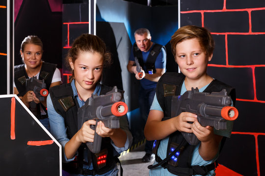 teen brother and sister with laser pistols playing laser tag with their parents