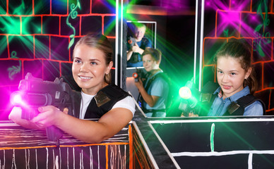 Fototapeta na wymiar Positive girl with laser gun having fun on laser tag arena with