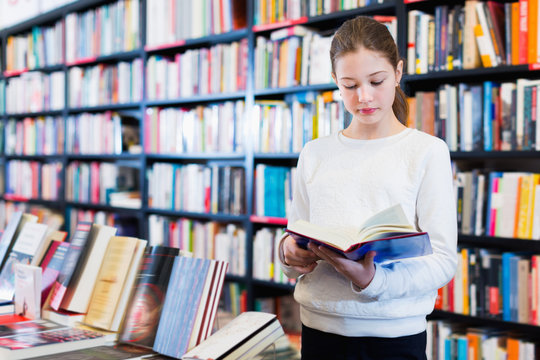 Intelligent preteen girl standing alone near bookcase in library