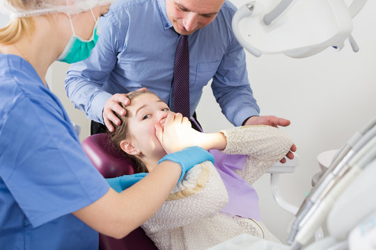 Frightened girl in dental chair refusing to open mouth