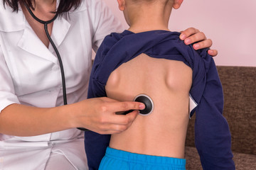 Pediatrician listening boy's breathing with stethoscope on back
