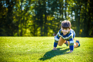 Caucasian boy climbs up on fresh green grass meadow, happy kids enjoying peaceful summer weekend outdoors. Friendship relaxation concept